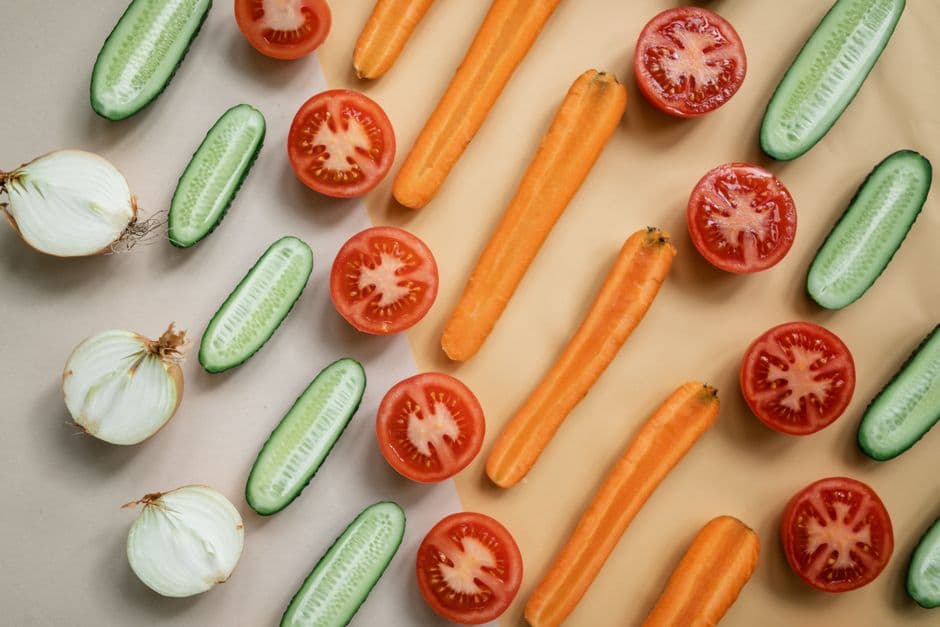 Flat lay of fresh sliced vegetables — carrots, cucumbers, onions and tomatoes — used to calculate calories and macros per serving with the recipe nutrition calculator